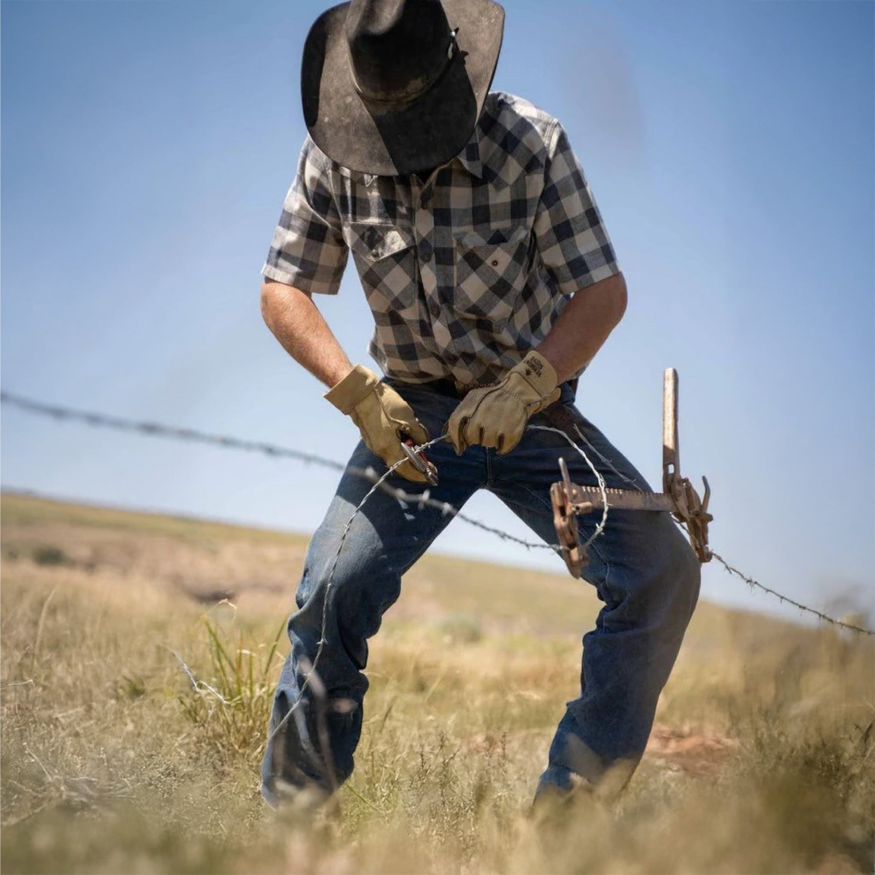 A man is working on farm field fence wire 